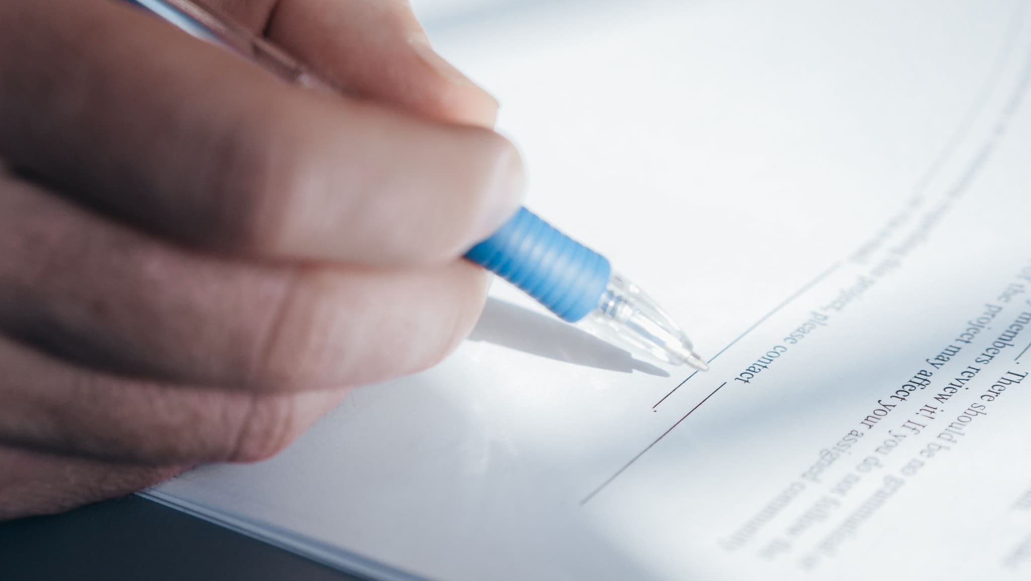 A hand steadies a pen over an official document, mid-signature, at the notary desk.