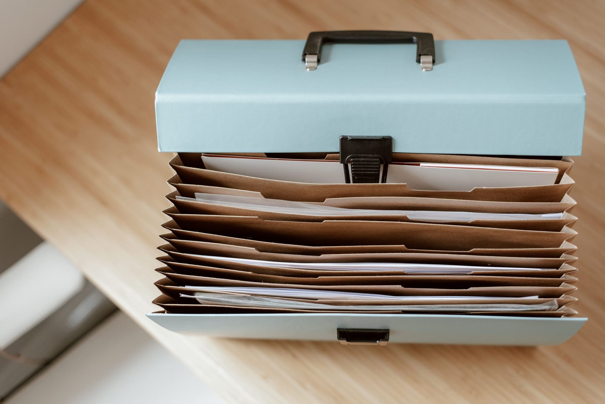 An open document case with papers on a wooden desk in daylight, ready to be filed.